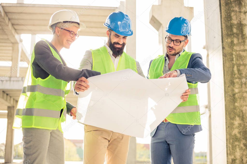 Mixed group of engineers or business partners at construction site, working together on building's blueprint. Architecture and teamwork concept.