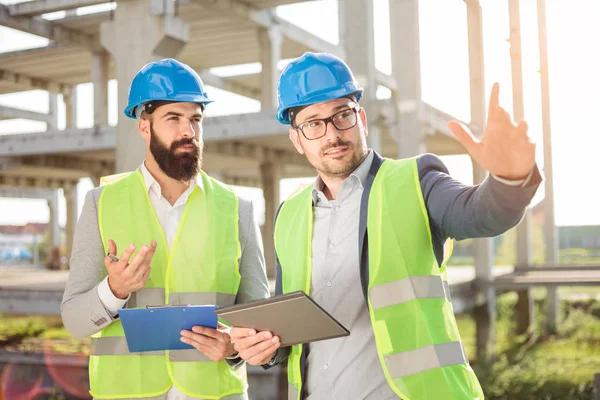 Dos jóvenes arquitectos masculinos o socios de negocios hablando en una obra de construcción — Foto de Stock