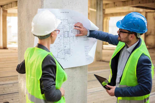 Dos jóvenes arquitectos exitosos mirando planos en un sitio de construcción — Foto de Stock