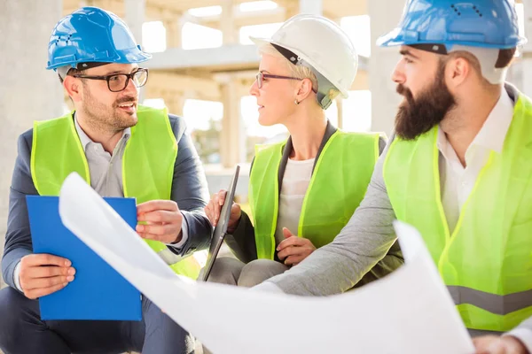 Pequeño equipo de arquitectos visitando un sitio de construcción, mirando los planos — Foto de Stock