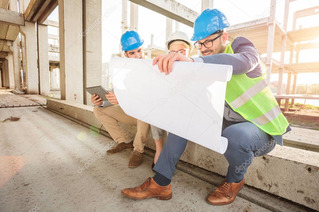 Group of young architects looking at floor plans during inspection of a construction site