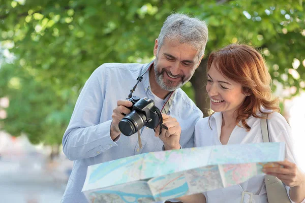 Dos turistas adultos caminando por el parque, la mujer sostiene un mapa y el hombre muestra imágenes en una cámara digital — Foto de Stock