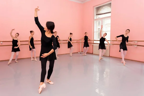 Mature female ballet teacher demonstrating dancing moves in front of a group of young teenage girls