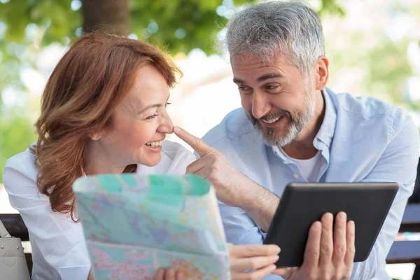 Bir bankta oturan, bir tablet üzerinde çalışan ve şehir haritasına bakan oyuncu olgun turistler. Kocası karısının burnuna dokunuyor, onunla alay ediyor.