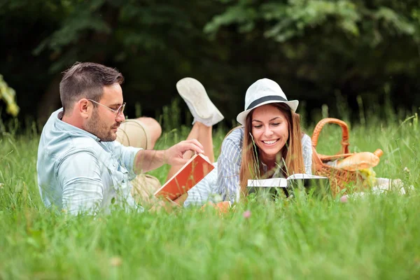 Pareja joven tumbada en una manta de picnic, leyendo libros y relajándose — Foto de Stock