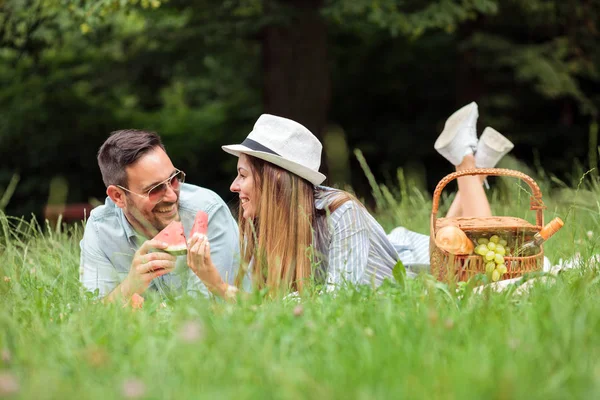 Pareja joven acostada en una manta de picnic, comiendo mellón de agua y relajándose — Foto de Stock