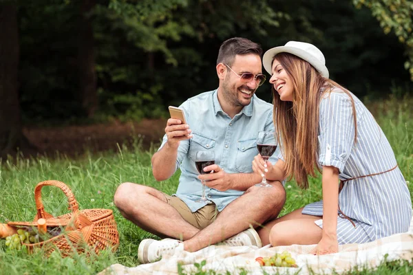Preciosa pareja joven que se divierte en un picnic en el parque, beber vino tinto y relajarse — Foto de Stock