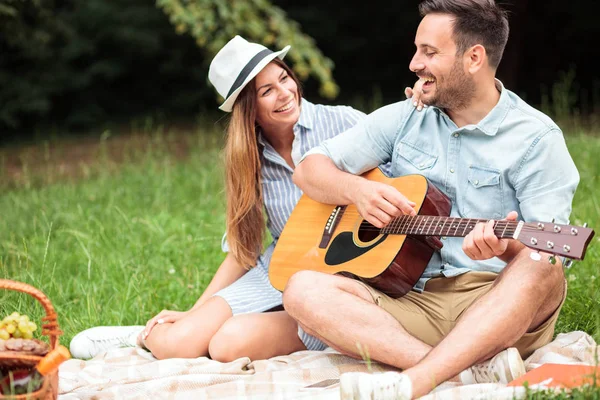 Romántica pareja joven pasando un buen rato en un picnic, tocando la guitarra y cantando — Foto de Stock