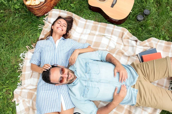 Pareja joven y romántica relajándose en un parque. Acostados boca arriba en una manta de picnic, abrazados — Foto de Stock