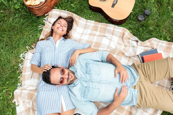 Romantik genç çift bir parkta rahatlatıcı. Piknik battaniyesi üzerinde sırtüstü yatmış, sarılmak