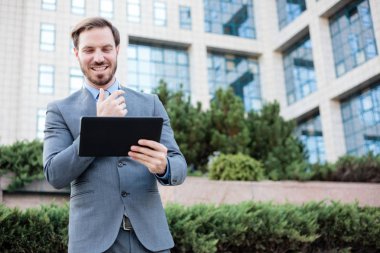 Bir ofis binasının önünde bir tablet üzerinde çalışan mutlu genç işadamı