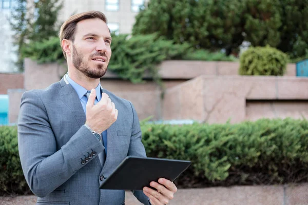 Επιτυχημένος νέος επιχειρηματίας που δουλεύει σε ένα δισκίο μπροστά από ένα κτίριο γραφείων. Κρατώντας χέρι στο πηγούνι και κοιτάζοντας σε απόσταση — Φωτογραφία Αρχείου