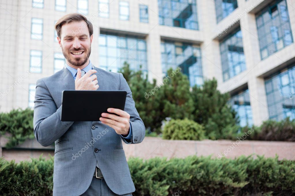 Happy young businessman working on a tablet in front of an office building