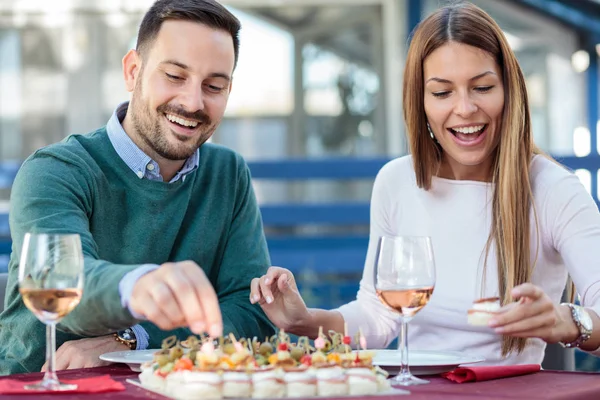 Feliz pareja joven disfrutando de aperitivos y beber vino rosa antes del almuerzo —  Fotos de Stock