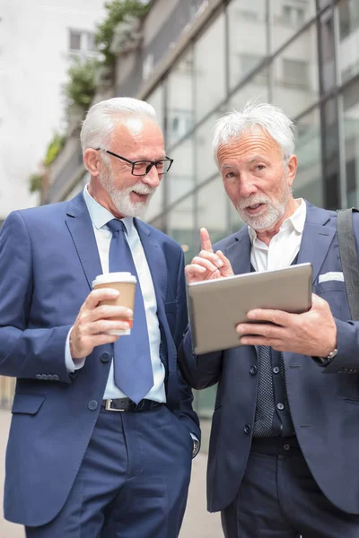 Two senior gray haired businessmen talking in front of an office building — Stock Photo, Image