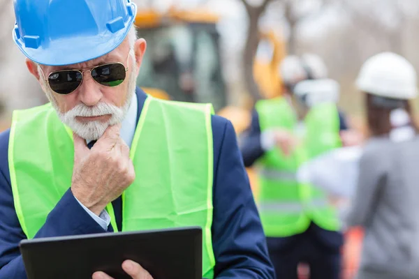 Ingeniero serio, preocupado, de pelo gris senior o hombre de negocios que trabaja en una tableta en el sitio de construcción — Foto de Stock
