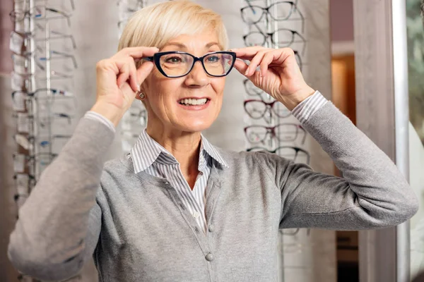 Lächelnde Seniorin probiert Brille im Optikergeschäft aus — Stockfoto