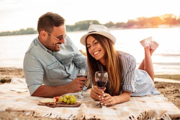 Hermosa pareja joven disfrutando de un picnic en una playa —  Fotos de Stock