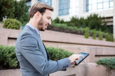 Bir ofis binası önünde bir tablet üzerinde çalışan yakışıklı genç işadamı