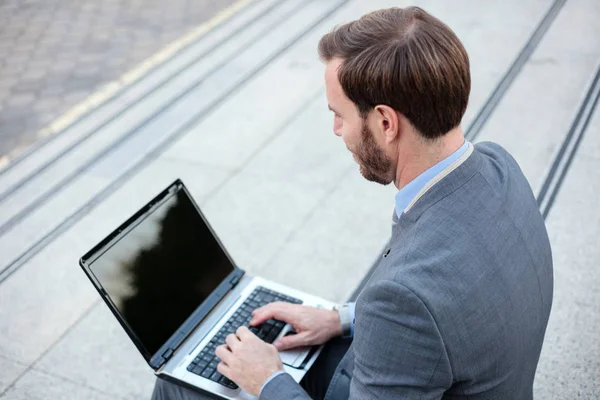 Όμορφος νέος επιχειρηματίας που δουλεύει σε ένα φορητό υπολογιστή μπροστά από ένα κτίριο γραφείων. Προβολή υψηλής γωνίας — Φωτογραφία Αρχείου