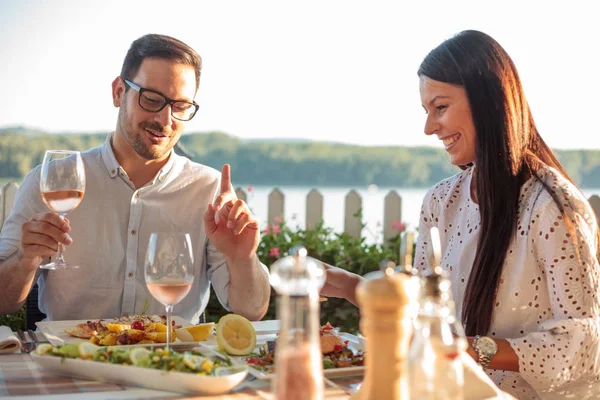 Feliz joven pareja comiendo pescado cena en restaurante junto al río —  Fotos de Stock