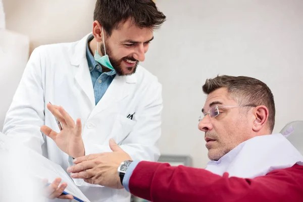 Hombre adulto medio consultando con dentista joven durante el examen en la clínica dental —  Fotos de Stock