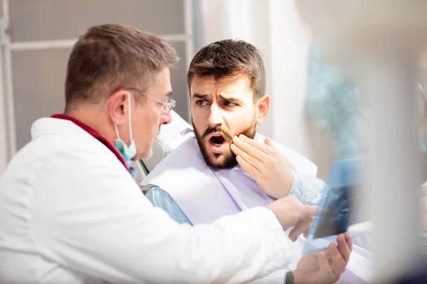Joven con dolor de muelas consultando con un dentista masculino durante el examen en la clínica dental —  Fotos de Stock