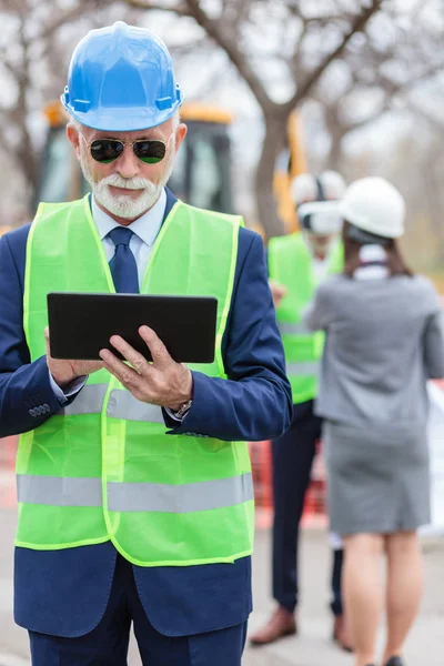 Retrato de cerca del hombre de negocios o ingeniero de pelo gris senior que trabaja en una tableta mientras visita el sitio de construcción — Foto de Stock