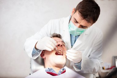 Genç erkek diş hekimi olgun erkek hasta muayene, çürük arıyor