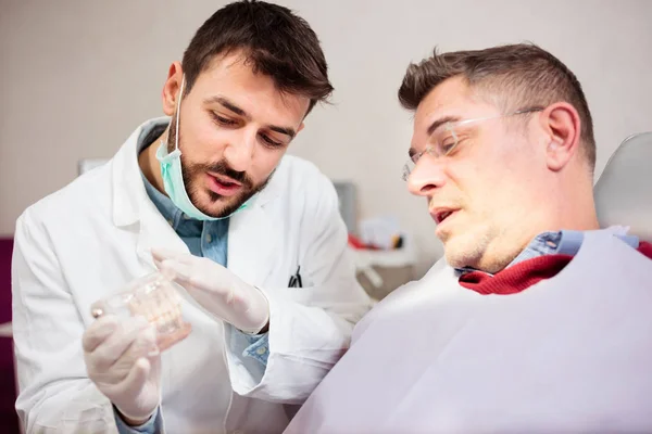 Joven dentista masculino mostrando modelo de encías y dientes para hombre maduro, consultando —  Fotos de Stock