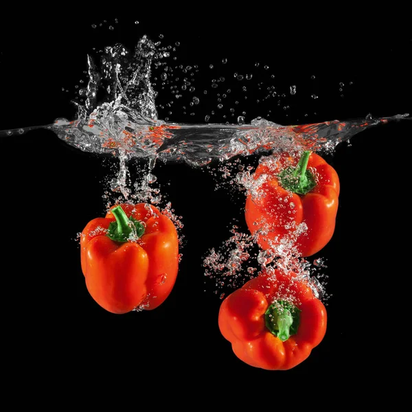 Three red bell peppers falling in water with splash on black background, paprika, stop motion photography