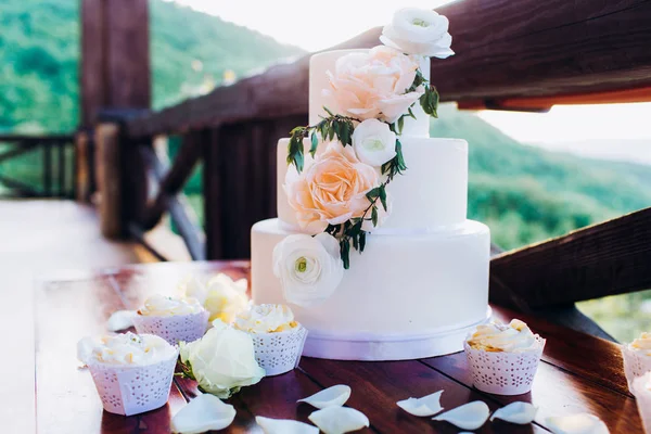 Weiße Hochzeitstorte mit Blumen auf einem Holztisch. — Stockfoto