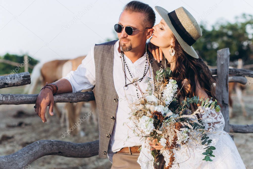 The groom dressed in the style of boho gently kisses the bride.