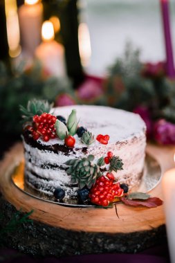 Çiçekler ve mumlarla çevrili narlı ve sulu bir düğün pastası..