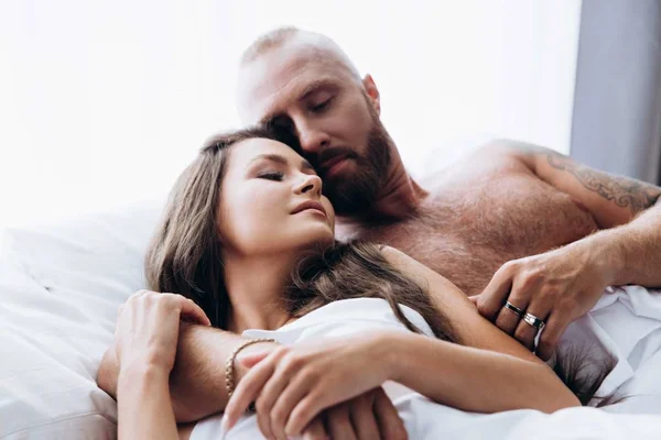 Um casal amoroso ri-se na cama. Sorrindo um para o outro em folhas brancas. — Fotografia de Stock