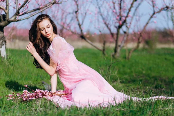 Fiatal lány egy rózsaszín virágos kertjében őszibarack rózsaszín ruhában és smink. — Stock Fotó