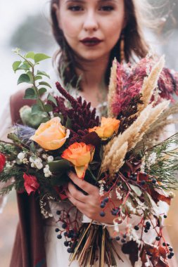 Sarı bir sonbahar çayırında düğün çiçekçisi. Boho tarzı giyinmiş bir kızın ellerinde..