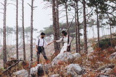 Sakallı şık adam boho tarzında bir elbise giymiş bir kız kucaklar. 