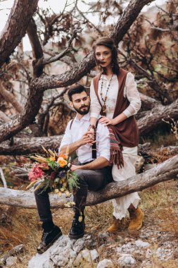 Sakallı şık adam boho tarzında bir elbise giymiş bir kız kucaklar. 