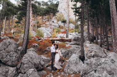 Sakallı şık adam boho tarzında bir elbise giymiş bir kız kucaklar. 