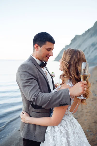 Feliz casal recém-casado. Bela noiva e noivo em um terno com champanhe em um contexto de montanhas . — Fotografia de Stock
