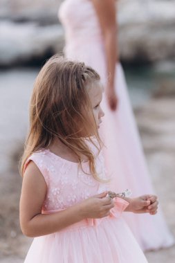 Anne ve kızı bir uçurumda ve pembe elbiseler içinde denize bakmak. 