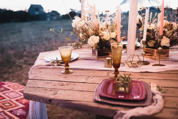 Romantisk middag av bruden och brudgummen på ett träbord med vinröda tallrikar och färska blommor. — Stockfoto