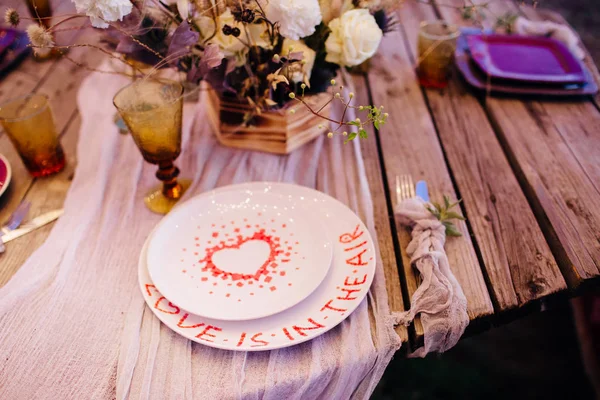 Dîner romantique sur une table en bois avec assiettes bordeaux et fleurs fraîches . — Photo