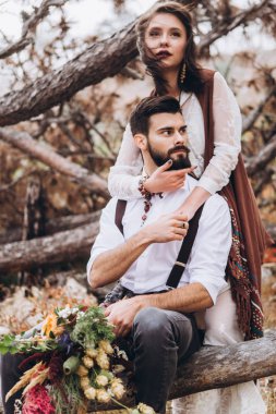 Sakallı şık adam boho tarzında bir elbise giymiş bir kız kucaklar. 