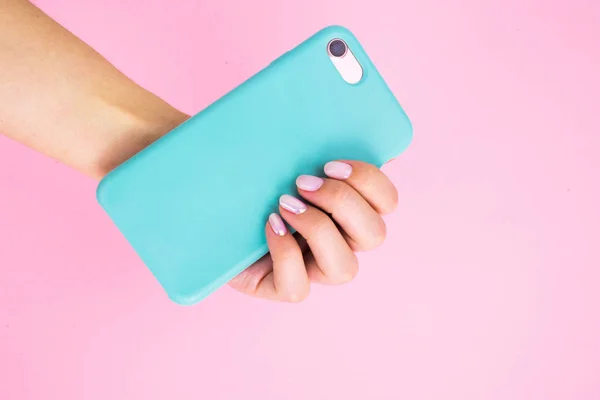 Smartphone in a mint case in hand with manicure on a pink background.