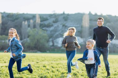 Mutlu aile tarlada koşuyor. Baba, anne ve çocuklar yeşil bir tarlada koşuyor..
