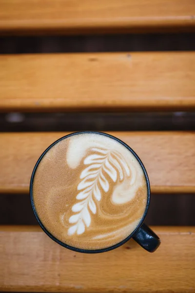 Coupe de cappuccino avec un motif sur un banc en bois. — Photo