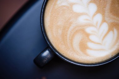 Bir bardak kapuçino, ahşap bir bankta desenli..