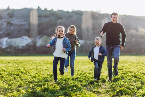 Far, mor och barn springer genom ett grönt fält. — Stockfoto